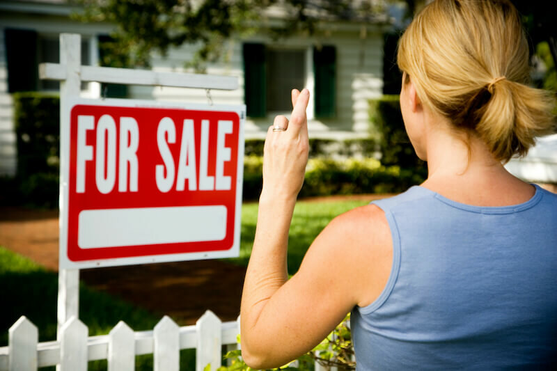Woman standing by a for sale sign outside an inherited house